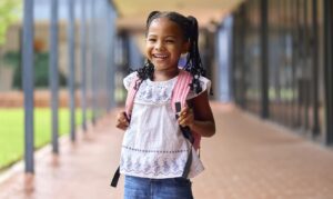 Retrato de uma aluna sorridente da escola primária do sexo feminino ao ar livre com mochila na escola